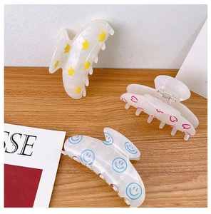 Detailed close-up of shell-shaped acrylic hair claws with cute smile and heart patterns