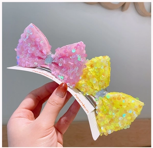 Detailed close-up of pink and yellow sequined bow hair clips on fashion card