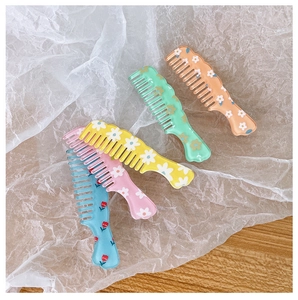 Close-up of five colorful floral hair combs in pastel orange, green, yellow, pink, and blue