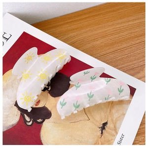 Detail of acrylic hair claws with sun and tulip prints on a magazine background