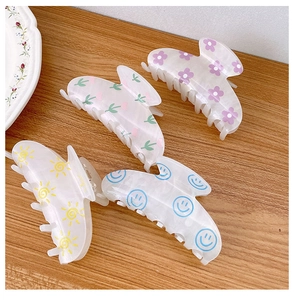 Detail view of four shell-shaped acrylic hair claws with cute floral and smile patterns
