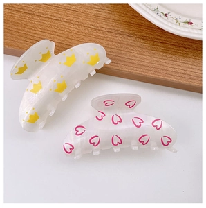 Detail view of two acrylic hair claws featuring yellow crowns and pink heart patterns