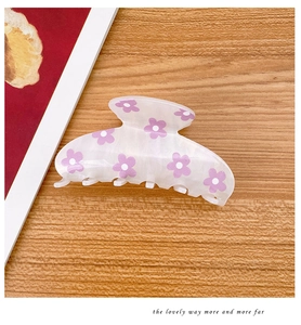 Detail of a creamy translucent hair claw clip with purple floral patterns on wood