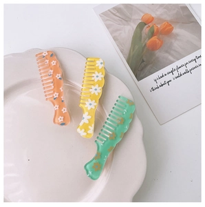 Detail of three floral mini hair combs in orange, yellow, and mint green acrylic