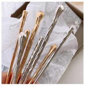 Detailed macro view of liquid metal hair pins with unique wavy texture in gold and silver