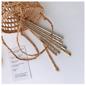 Close-up of golden and silver metal hair pins with unique hammered texture on white surface