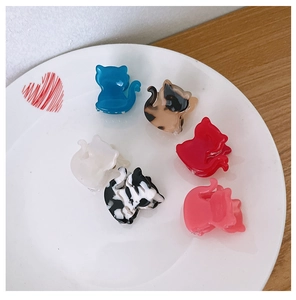 Set de seis mini pinzas para el cabello con forma de gato de colores sobre un plato