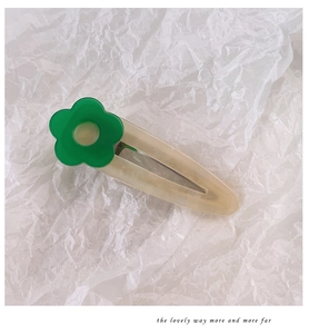 Detailed close-up of a cream acetate hair clip with a green flower on textured paper