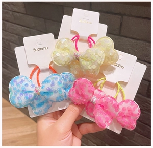 Dettaglio di elastici per capelli con fiocchi glitterati blu, rosa e gialli per bimbe