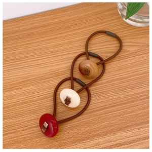 Three elastic hair ties with colorful resin buttons and gold details on wood surface