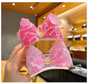 Vue détaillée des nœuds à cheveux roses avec paillettes et fleurs en tissu 3D ornées