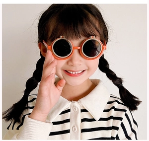 Dettaglio degli occhiali da sole rotondi arancioni per bambini con lenti scure su modello