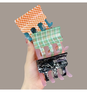 Detail view of acetate hair claws in checkerboard and marble patterns held by hand
