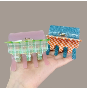 Detail of pink and green checkered acetate hair claw clips held by hand for scale
