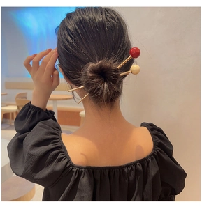 Detail view of red and cream resin beads on golden hair sticks in a classic bun hairstyle