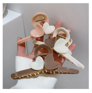 Three large acrylic heart hair claws in milk tea colors held in hand against white wall