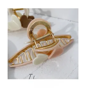 Detail of elegant milk tea pink claw clip with white heart motif and golden metal spring