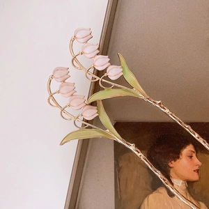 Detail of pink lily of the valley hair pin with gold stem and vintage floral art background