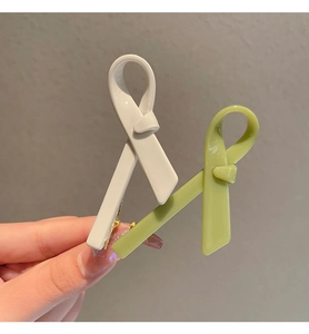 Detailed view of cream and green bow hair clips in hand with smooth acetate finish
