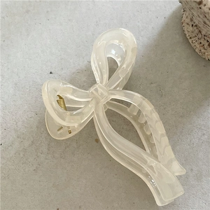 Detail of cream white bow hair claw with marble texture and gold metal spring
