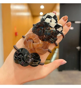 Close-up of four checkerboard and amber acetate hair ties held in hand for detail