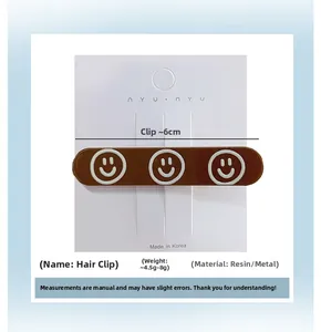 Close-up of 6cm brown hair clip with three white smiley faces on a display card