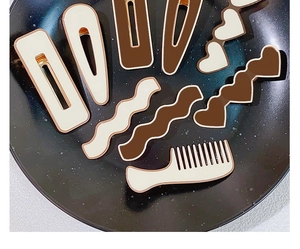 Detailed close-up of milk tea colored hair clips in various shapes on a black tray
