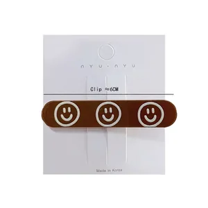 Brown 6cm hair clip with three white smiley faces on minimalist white background card