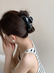 Grande pince à cheveux noire avec bordure blanche sur une coiffure mi-haute chic