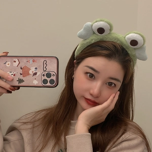 Close-up of a soft green plush headband featuring cute frog eyes and blue wings on model