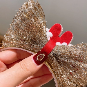 Détail d'un serre-tête de Noël avec un grand nœud doré pailleté et des bois rouges