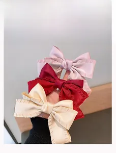 Detailed close-up of large satin bow hair clips in pink, burgundy, and beige colors