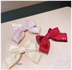 Close-up of three pleated satin bow hair clips in pink, red and beige colors