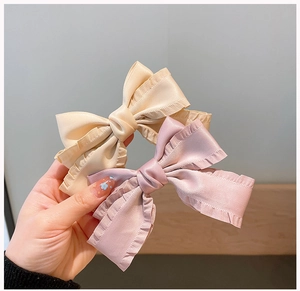 Close-up of handmade silk-like bow hair clips in beige and lilac with ruffle edges