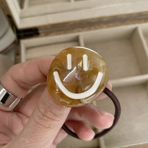 Close-up of a durable elastic hair tie with a retro smiley face amber resin charm