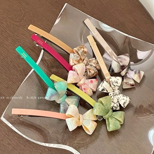 Elegant bow hair clips in assorted marble acetate colors on a glass tray over wood