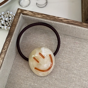 Detail shot of marble pattern hair tie with orange smiley face on wooden tray