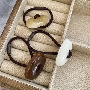 Three acrylic oval hair ties in beige, brown and white on a wooden display tray