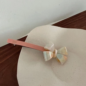 Detailed close-up of a pink marble texture acetate bow hair clip on a ceramic plate