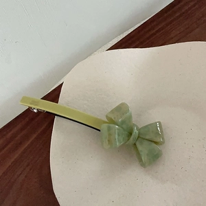 Detail of green marble pattern bow hair clip displayed on a white ceramic plate
