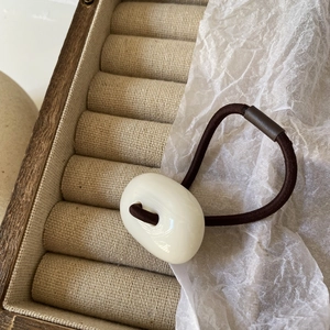 Close-up of white acrylic oval button hair tie on wood and cotton paper background