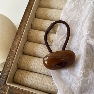 Detail view of a dark brown elastic hair tie with polished oval resin bead in a wood box
