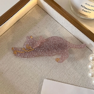 Close-up of a pink glitter cat hair clip with gold details on a decorative tray