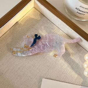 Detail of pink marble textured acetate cat hair clip with blue bow and gold accents