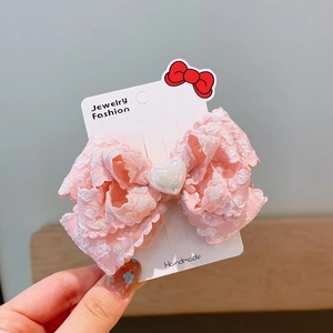Detailed view of a pink lace bow hair clip with a heart pearl on a display card