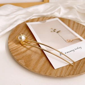 Close-up of golden U-shaped hair pin with hollow wire ball and large white pearl accent