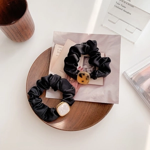 Dettaglio di due elastici in raso nero con fibbia quadrata in resina su vassoio legno