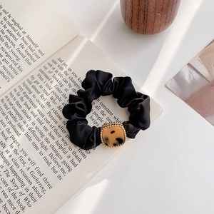 Dettaglio di elastico per capelli in raso nero con fibbia leopardata su libro aperto