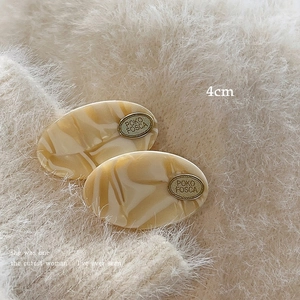 Macro detail of marble pattern acetate hair clip with gold metal logo on plush background