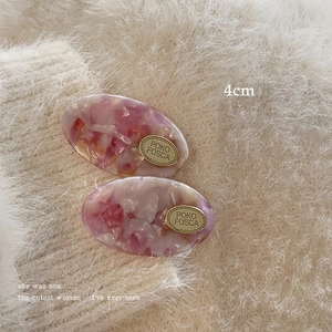 Close-up of pink marbled acetate hair clips with gold logo plate measuring 4cm